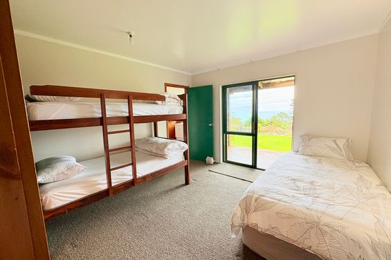 Bright bedroom featuring a King Single bed and bunk beds, with a private ensuite bathroom and large windows offering a sweeping sea view over the Hauraki Gulf.