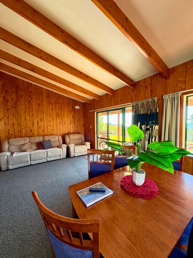 Indoor-outdoor flow at Ocean View Spa Retreat, Whitestar Station, featuring large stacker sliding doors opening from the dining area onto a deck with Hauraki Gulf views.