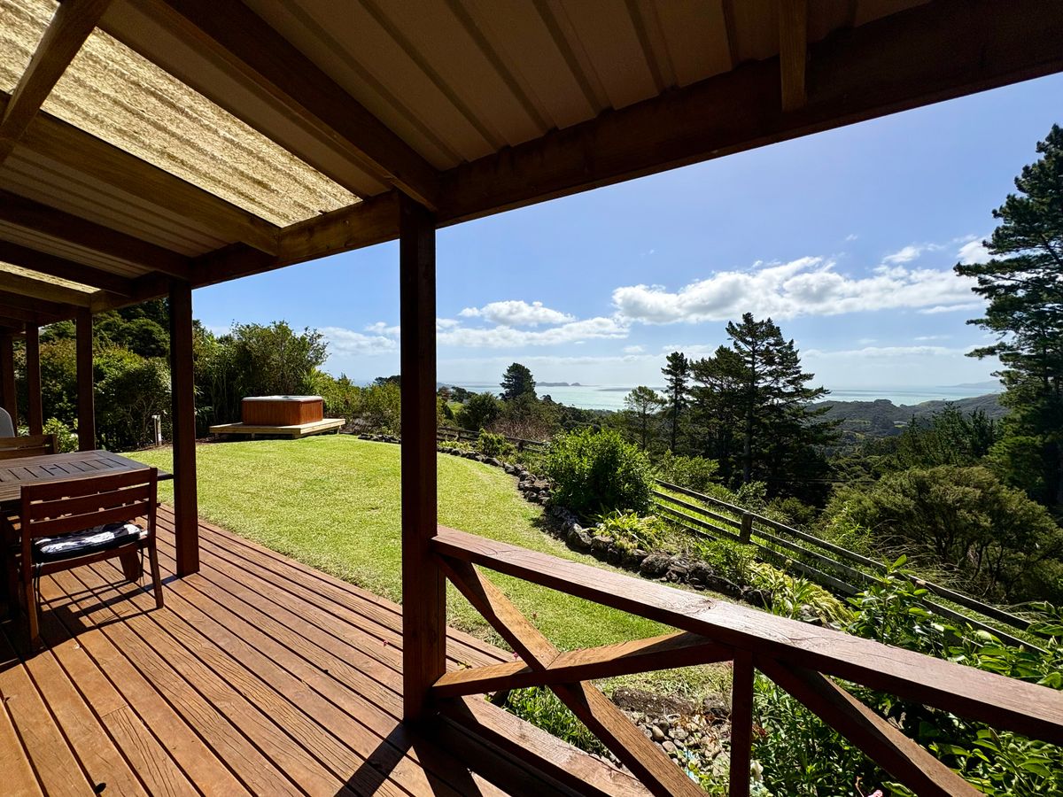 Spacious outdoor living area at Whitestar Station's premium cottage, featuring a large timber deck, outdoor dining, and a secluded spa pool overlooking the Coromandel coastline